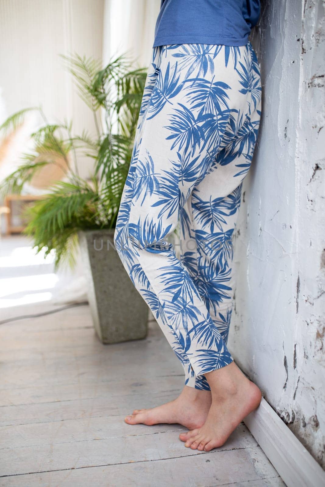 close-up of female legs in homemade blue pants with palm leaves.