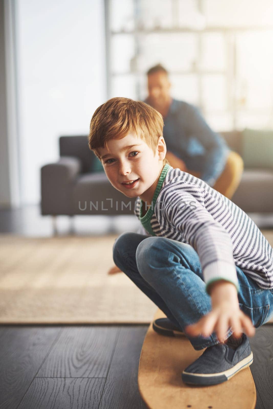 Lets go boarding. a cheerful little boy riding on a surfboard in the middle of the living room at home. by YuriArcurs