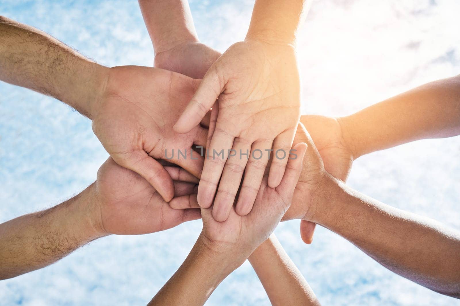 Hands in circle together, blue sky and community in collaboration for world support, trust and diversity. Teamwork, hand and summer sunshine, positive mindset and group of people in solidarity huddle.