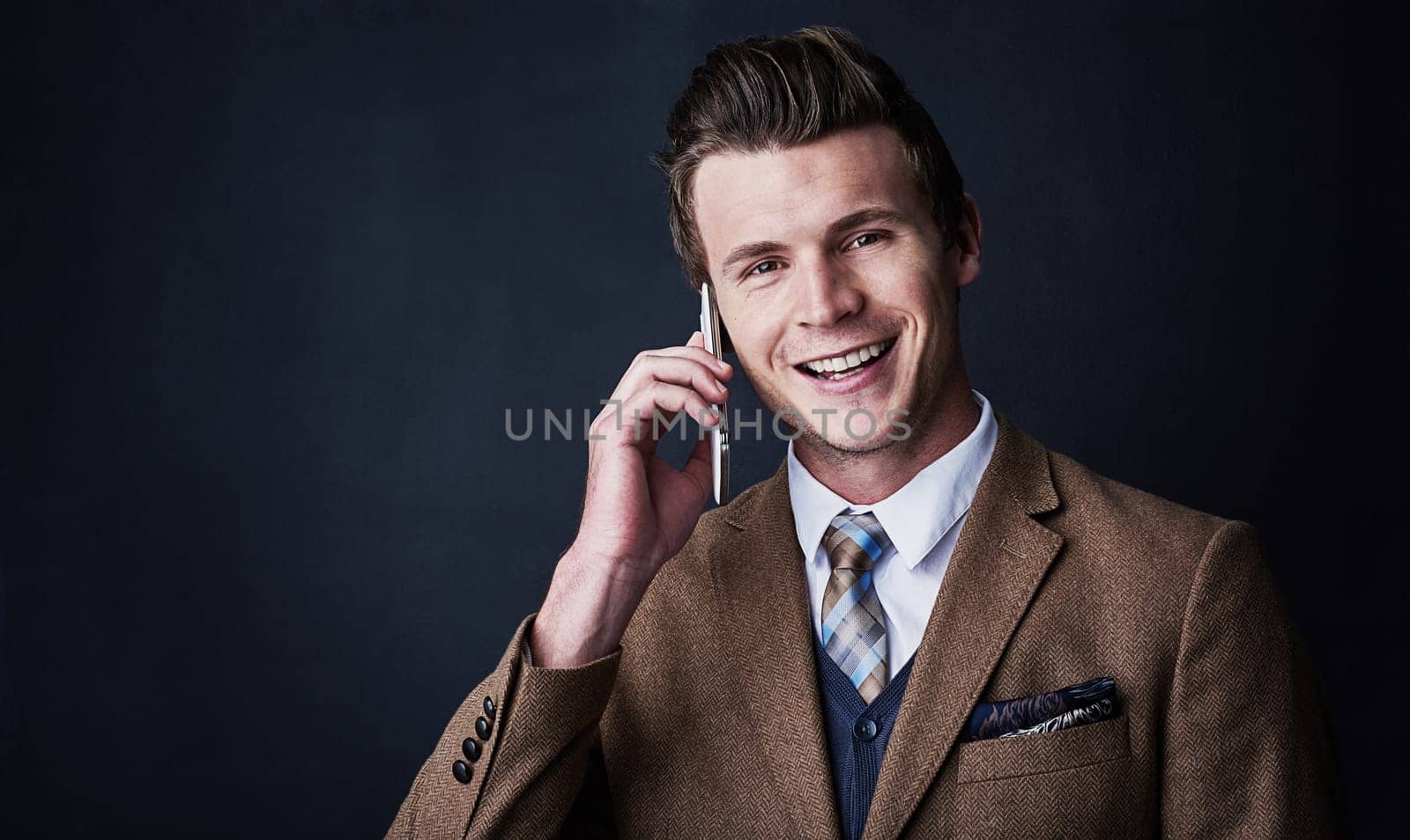 It feels good to be in business. Studio shot of a young businessman using his cellphone against a dark background. by YuriArcurs
