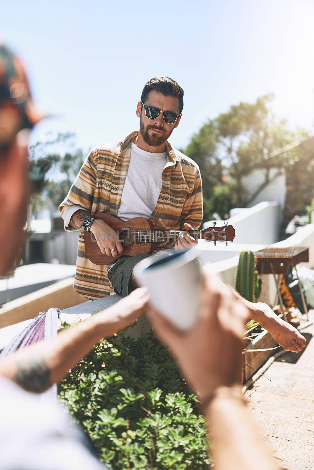 The one man band. a cheerful young man playing on his guitar while his friend listens outside on a balcony during the day