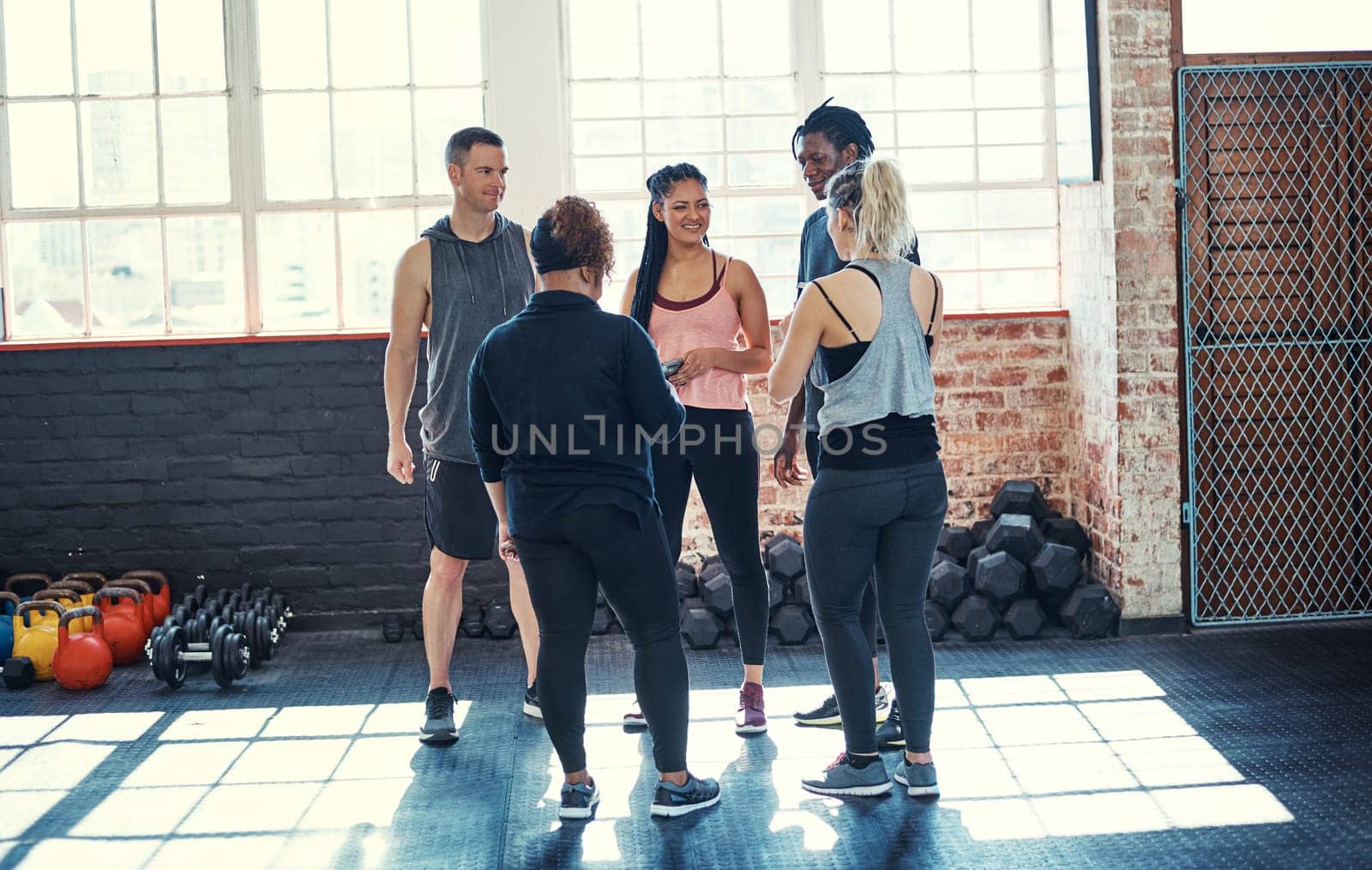 Everyone form a circle. a cheerful young group of people standing in a circle and having a conversation before a workout in a gym. by YuriArcurs
