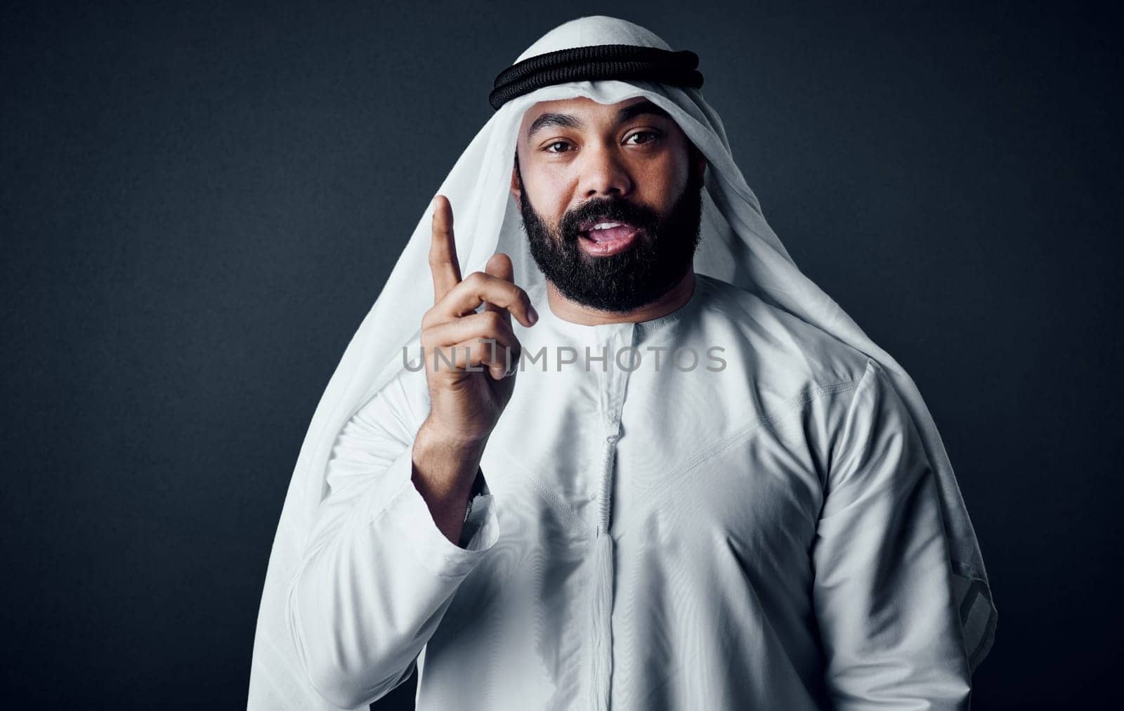 Do the things that scare you. Studio shot of a young man dressed in Islamic traditional clothing posing against a dark background. by YuriArcurs
