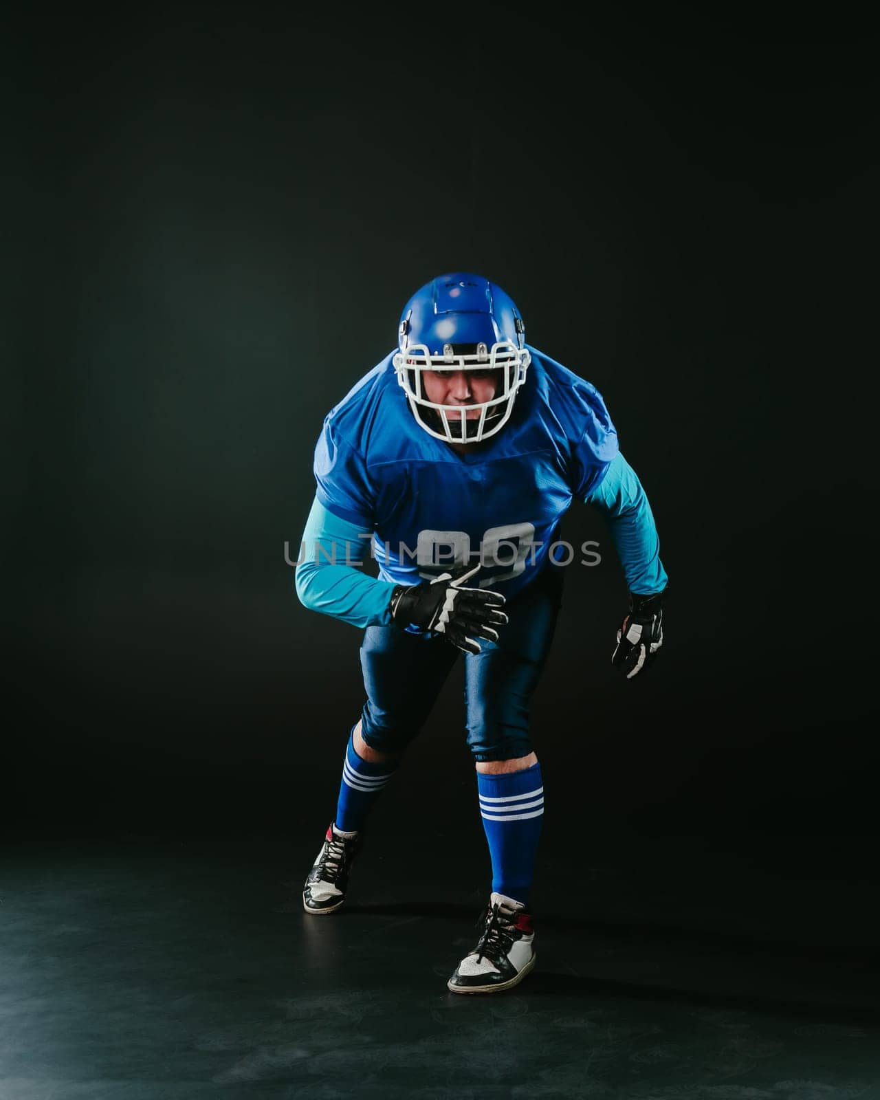 Portrait of a man in a blue uniform for american football runs with a ball on a black background