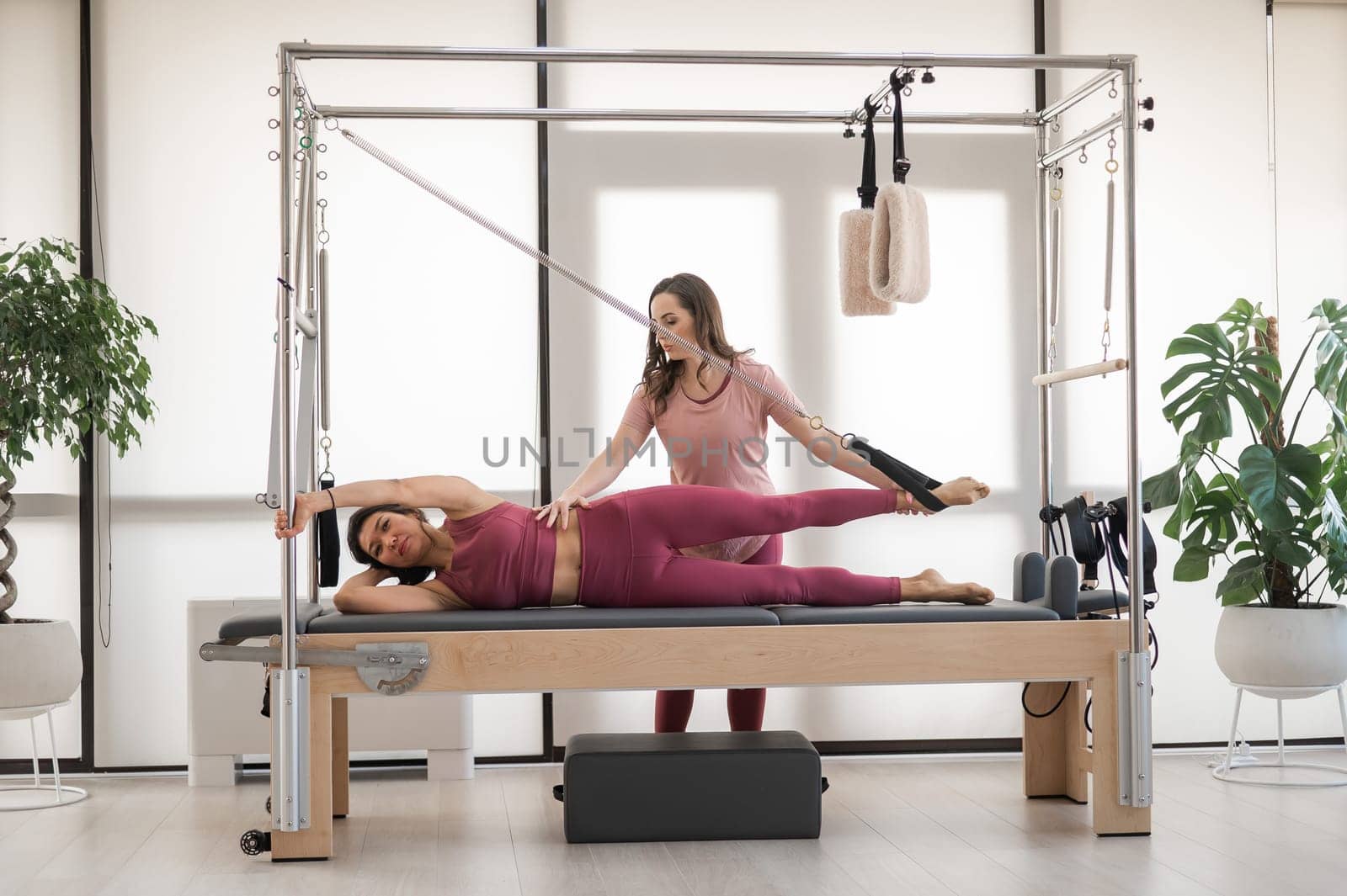 Asian woman doing pilates with trainer on cadillac reformer. by mrwed54