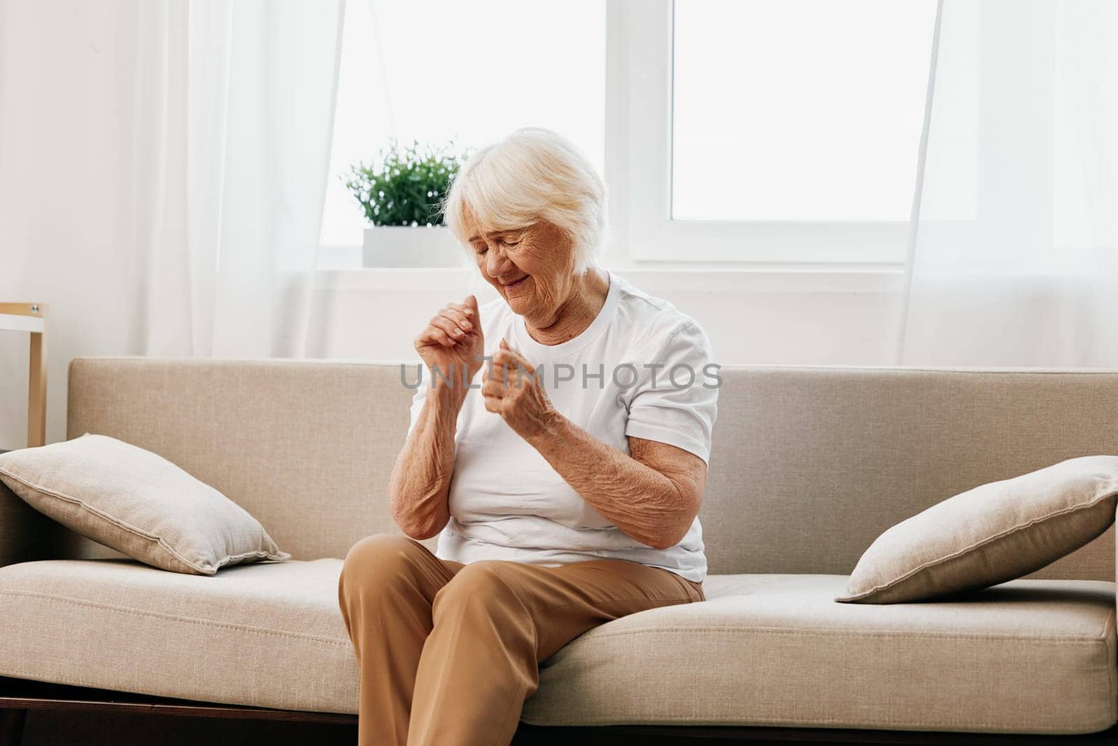 Elderly woman severe pain in the head sitting on the couch, health problems in old age, poor quality of life. Grandmother with gray hair holding her head, migraine and high blood pressure. High quality photo