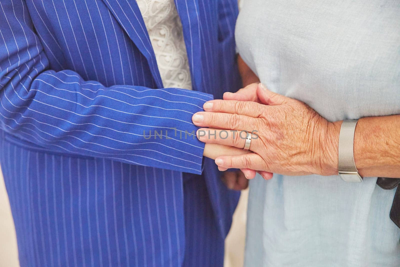 An elderly woman gently holds the hand of a young one. Close-up.