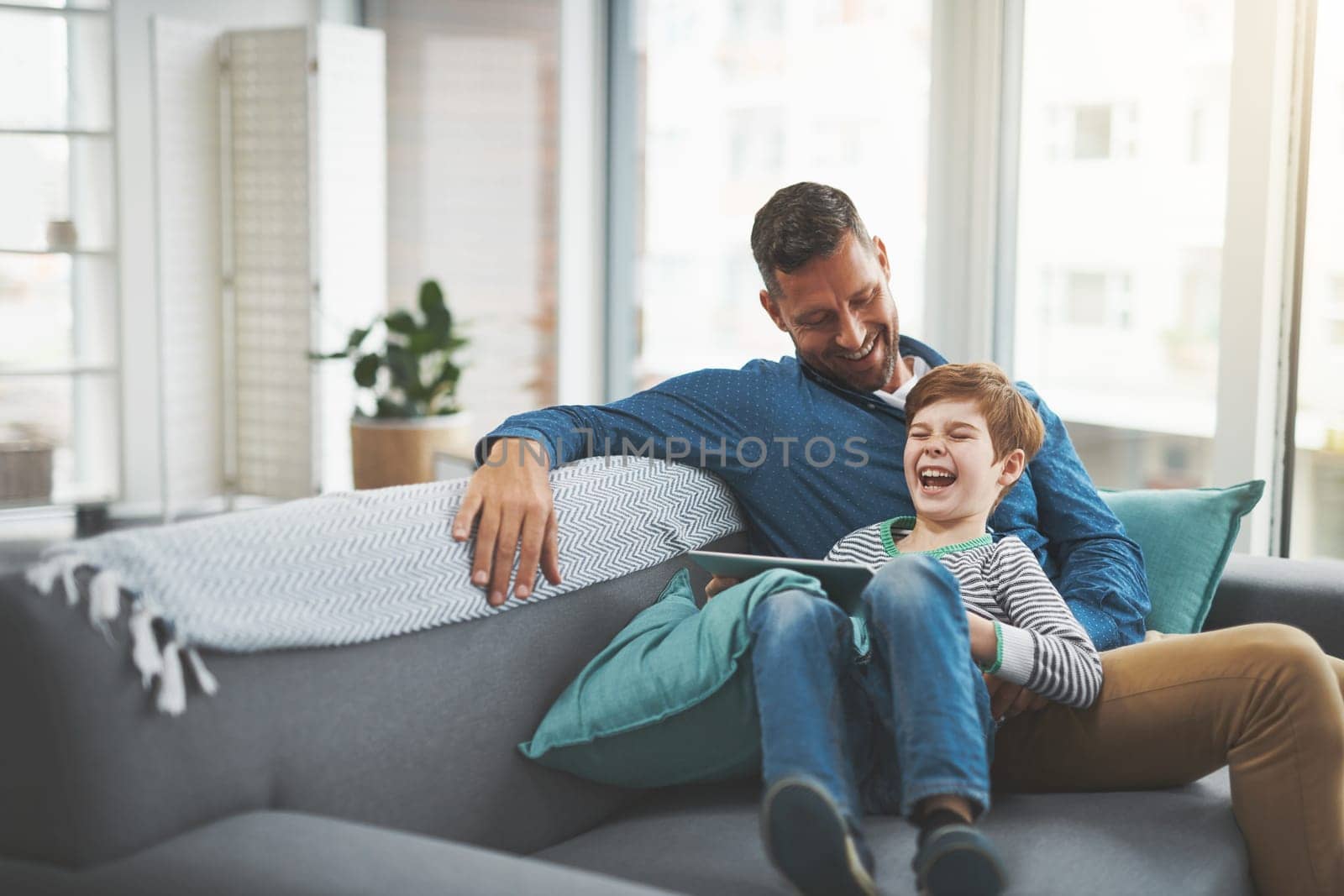 Keep your childrens minds captivated. a cheerful little boy browsing on a digital tablet while lying on his fathers lap at home during the day