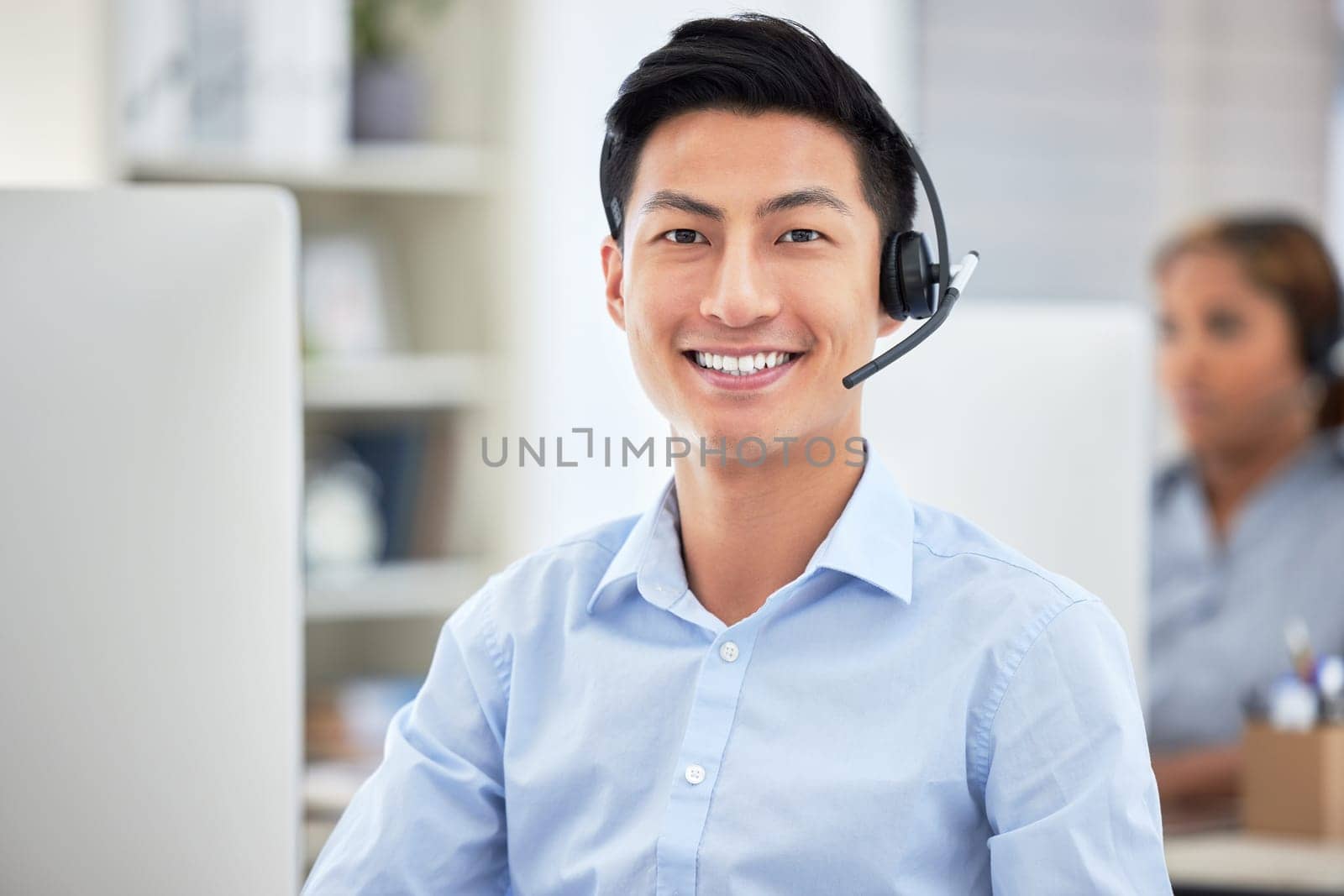 Portrait of asian call centre agent talking on headset while working on computer in office. Confident and smiling businessman consulting and operating a helpdesk for customer sales and service suppor.
