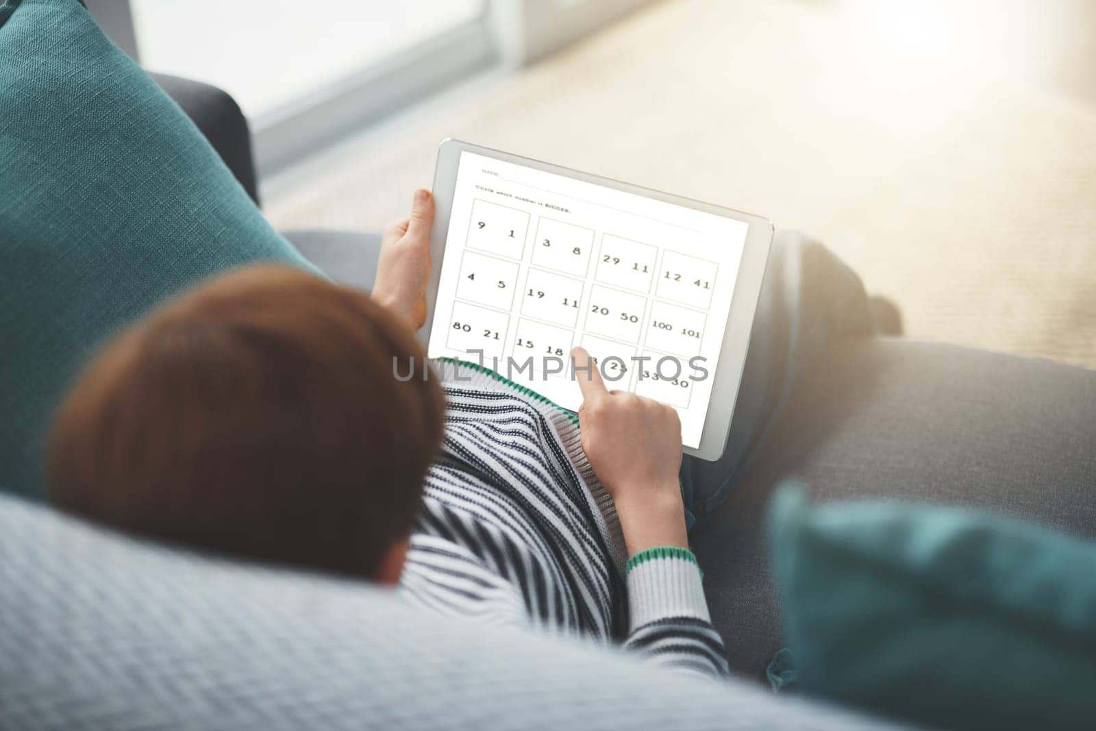 Doing some math in the morning. a focused little boy browsing on a digital tablet while being seated on a sofa at home during the day