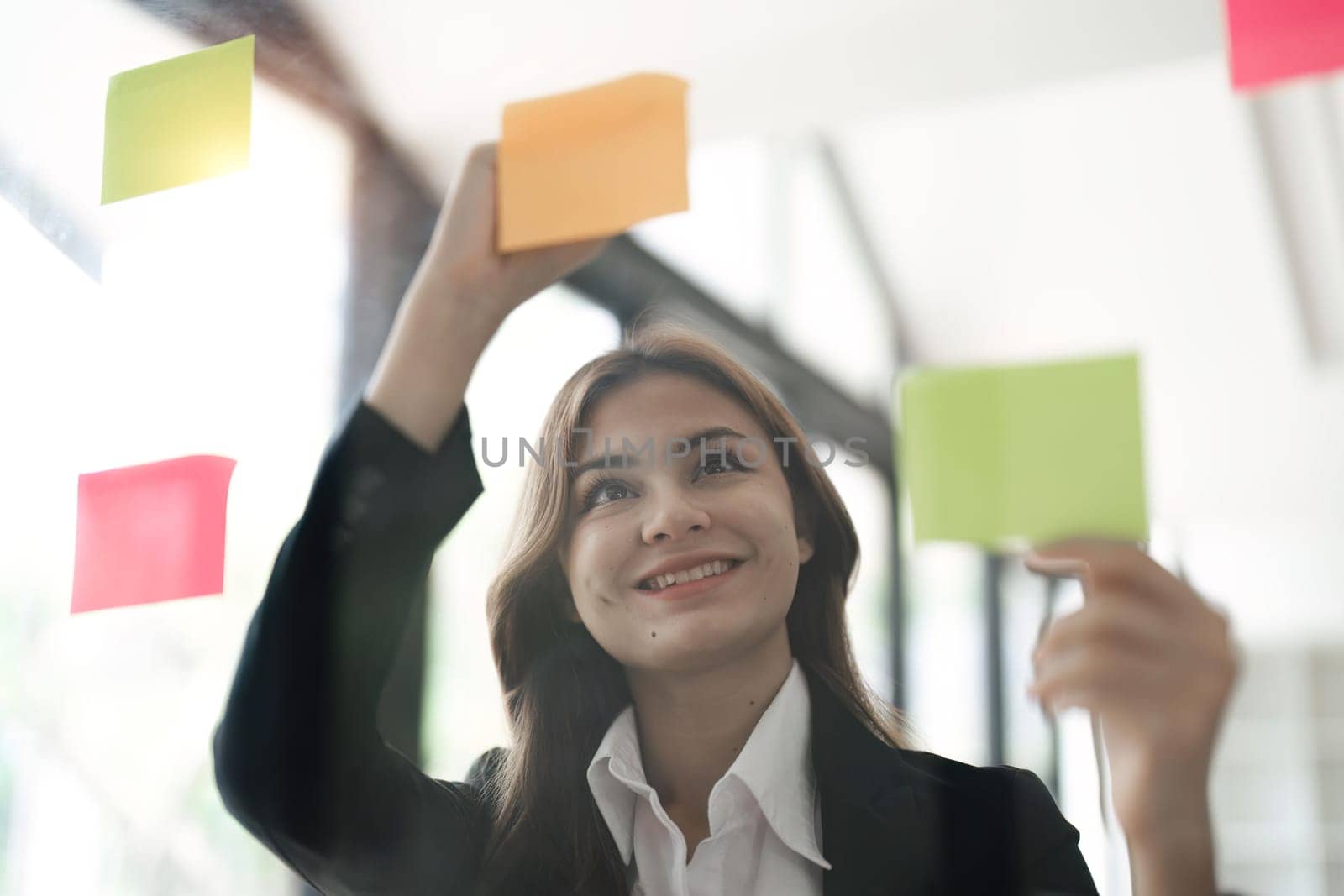 Asian businesswoman creating project plan on office wall with paper notes. Financial and Marketing projects.