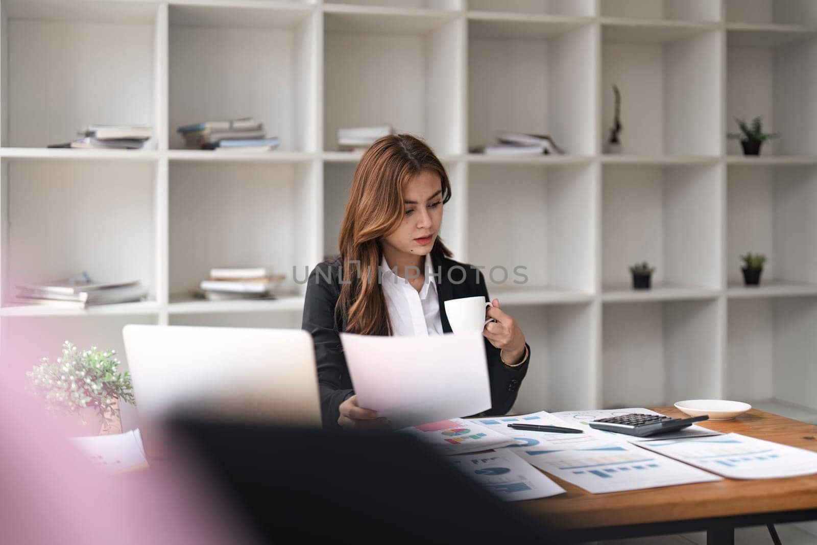 Serious young Asian business woman working with financial paperwork sitting in the office.