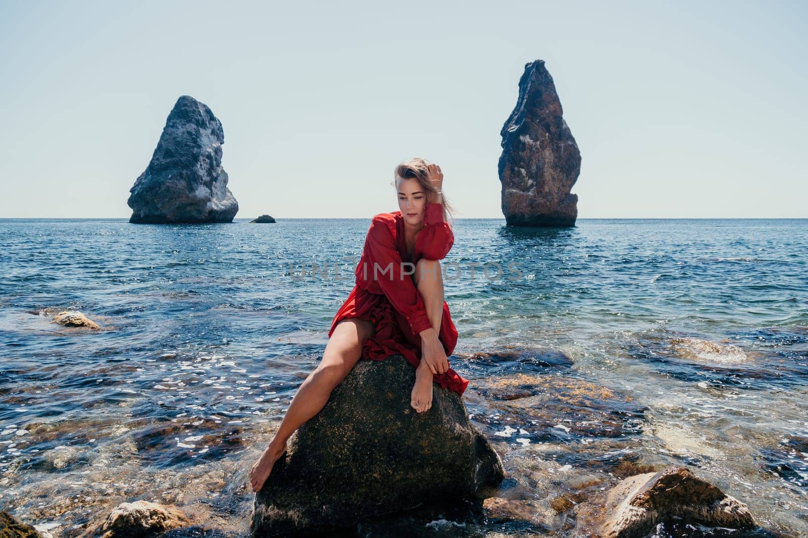 Woman travel sea. Young Happy woman in a long red dress posing on a beach near the sea on background of volcanic rocks, like in Iceland, sharing travel adventure journey