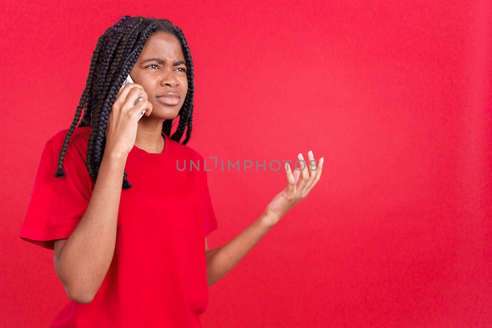 Angry african woman talking to the mobile in studio with red background