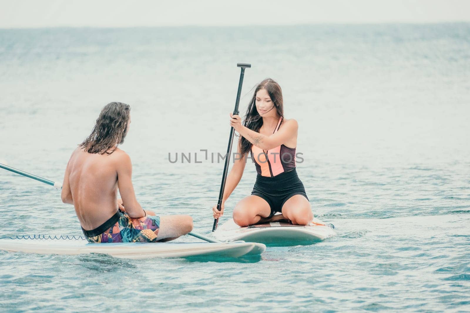 Sea woman and man on sup. Silhouette of happy young woman and man, surfing on SUP board, confident paddling through water surface. Idyllic sunset. Active lifestyle at sea or river