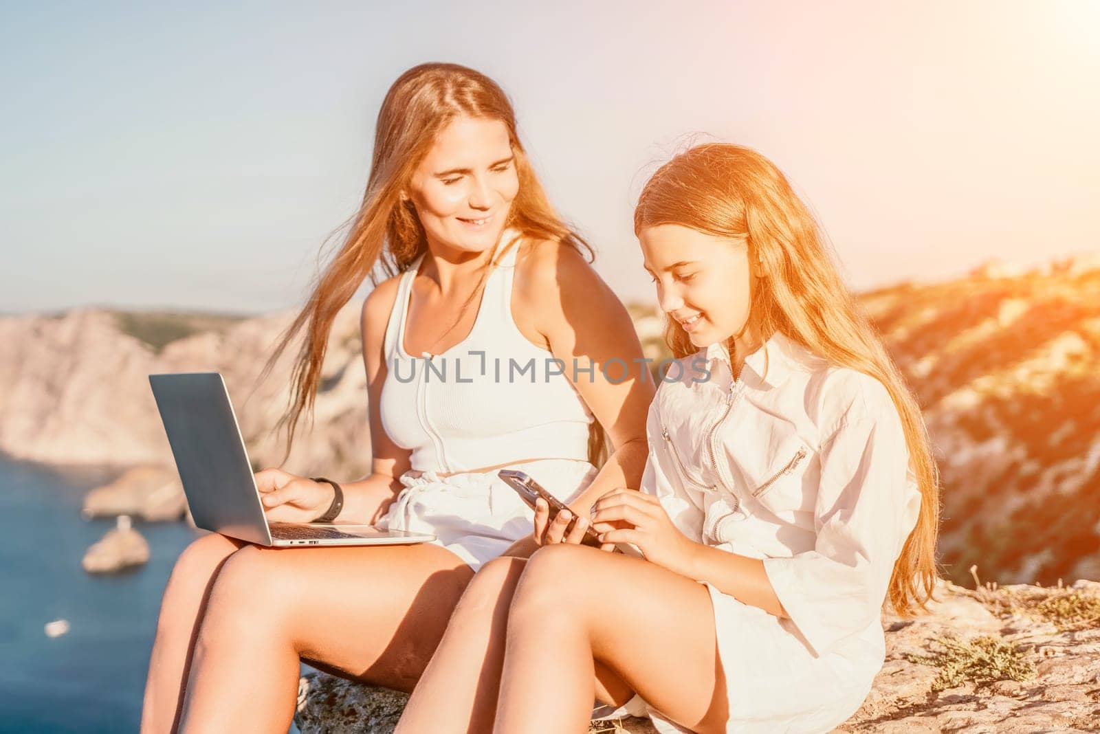 Successful business woman in yellow hat working on laptop by the sea. Pretty lady typing on computer at summer day outdoors. Freelance, travel and holidays concept.