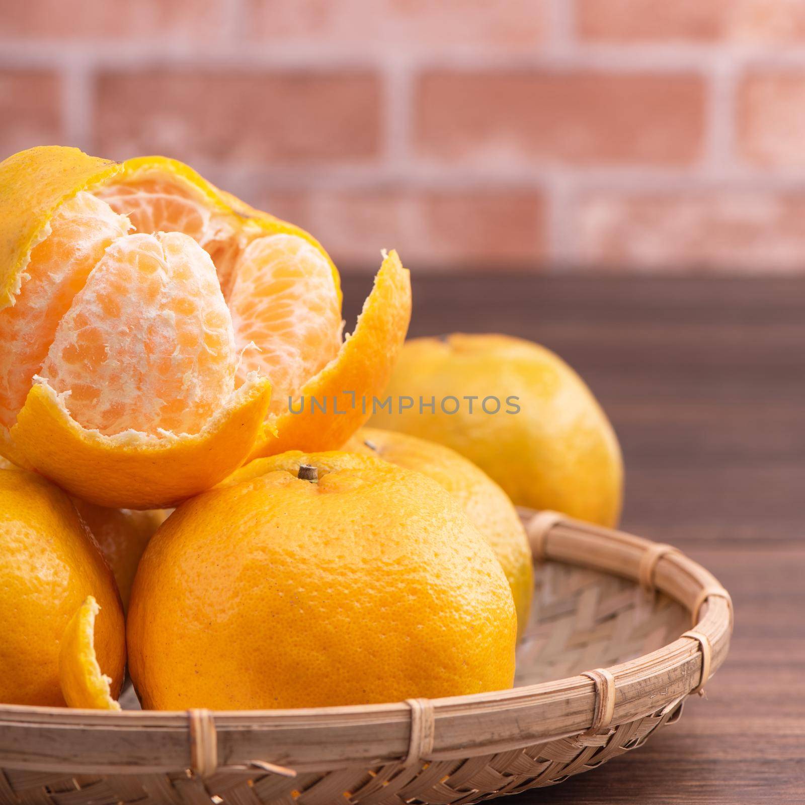 Peeled tangerines in a bamboo sieve basket on dark wooden table with red brick wall background, Chinese lunar new year fruit design concept, close up.