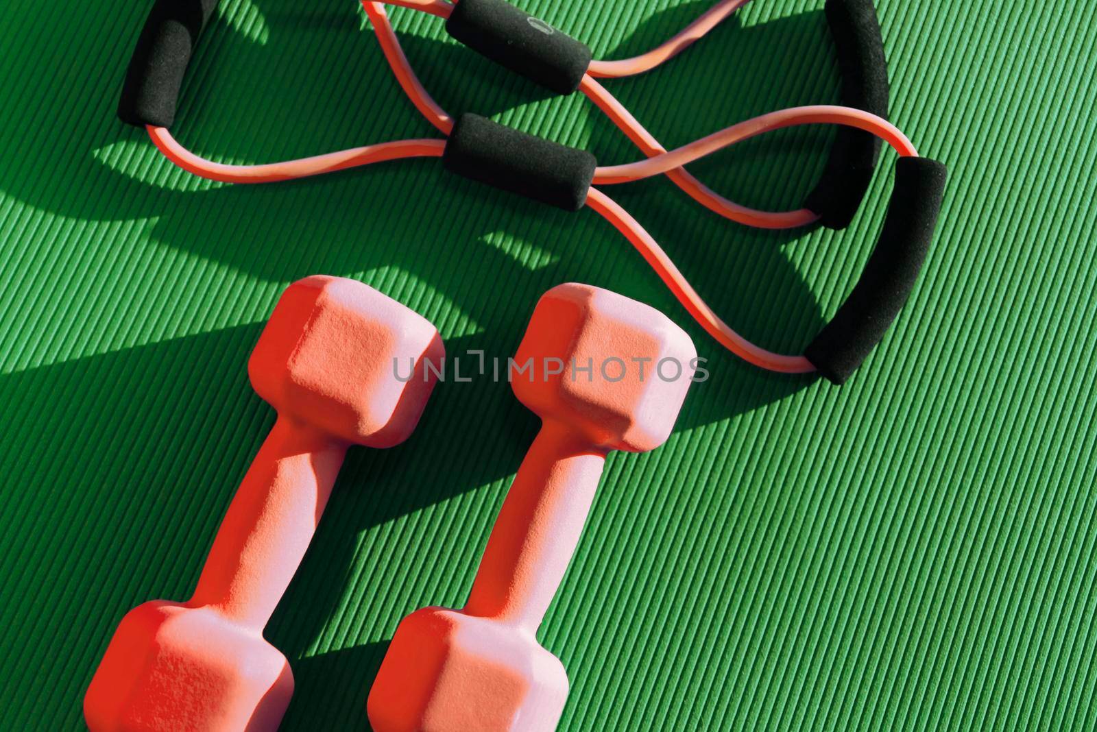 Top view of mat placed on wooden floor with bottle of water and smartphone near rubber expander in fitness club