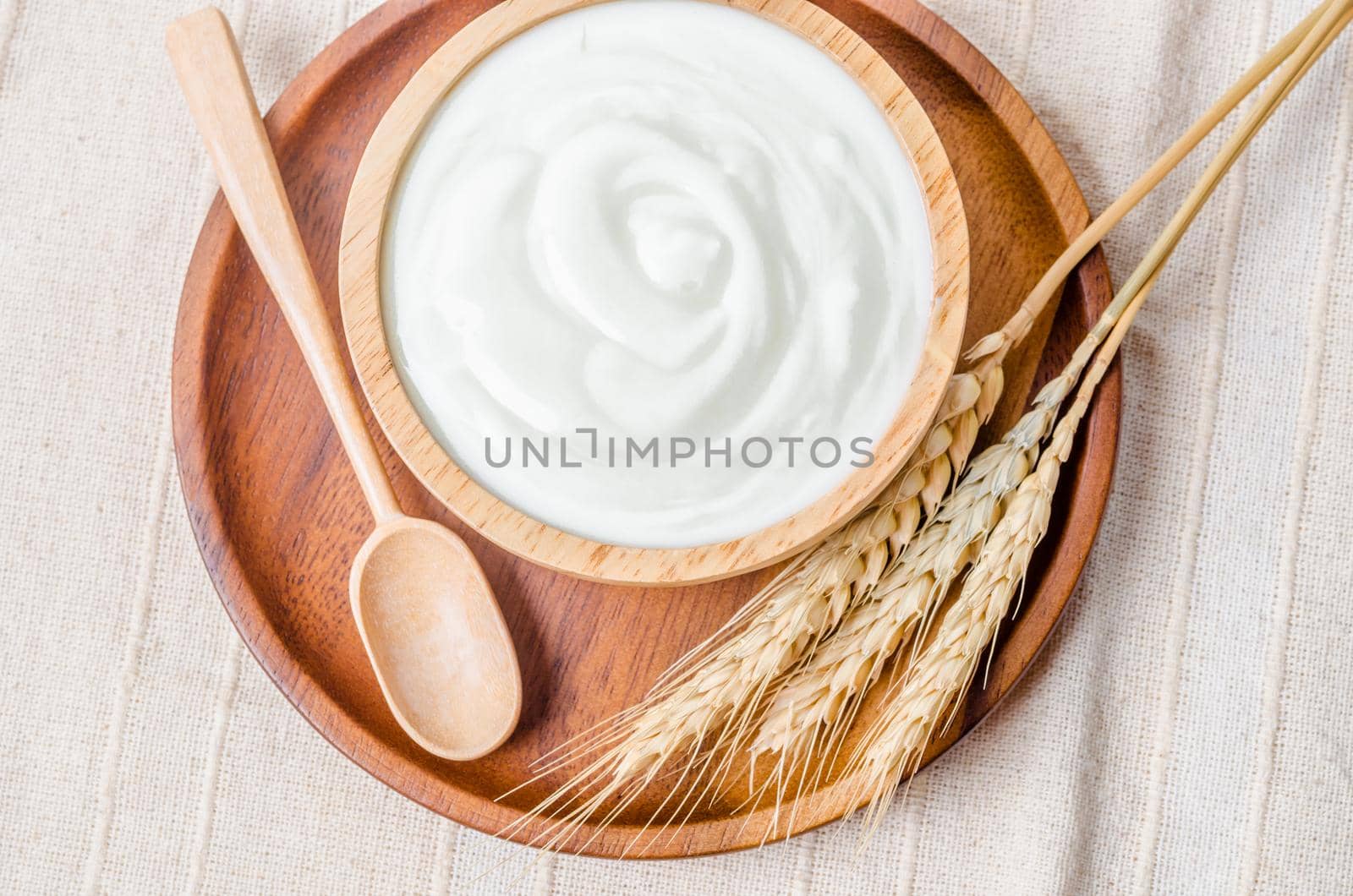 Greek yogurt in a wooden bowl and dry barley on tablecloth.