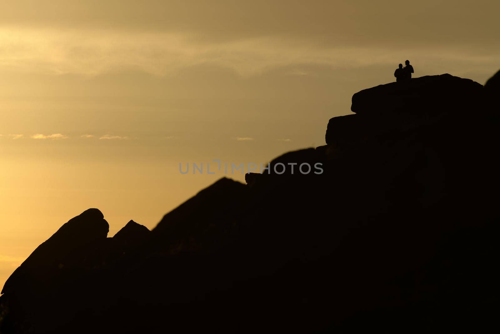 A couple stand silhouetted against a sunset atop stanage edge by RhysL