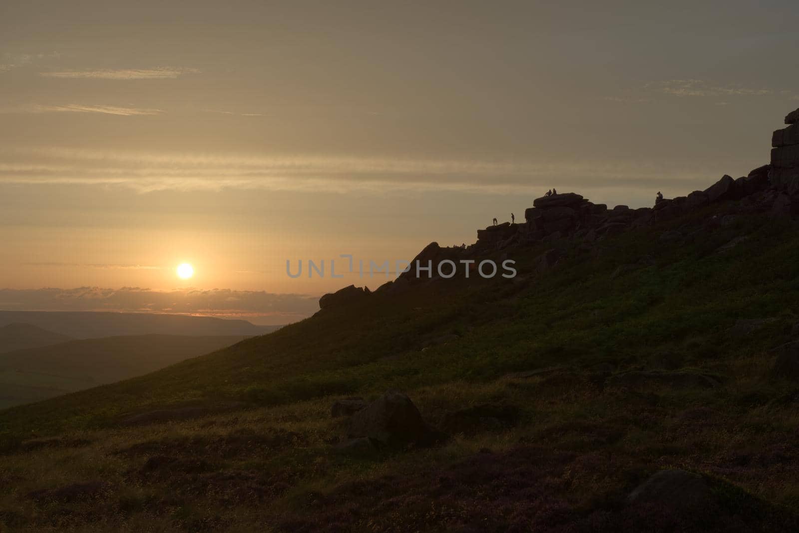 Climbers, couples and tourists line the rocky ridge of stanage edge at sunset. Many people enjoying the outdoors, wide angle perspective.