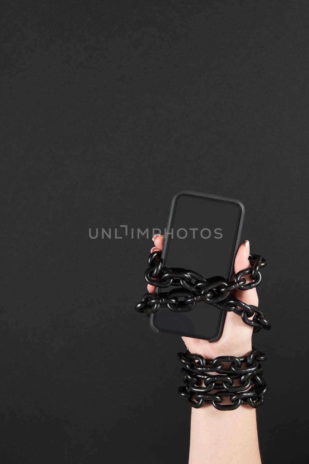 Iron chain that ties together hand and smartphone in concept of social media and internet addiction an black background by Mariakray