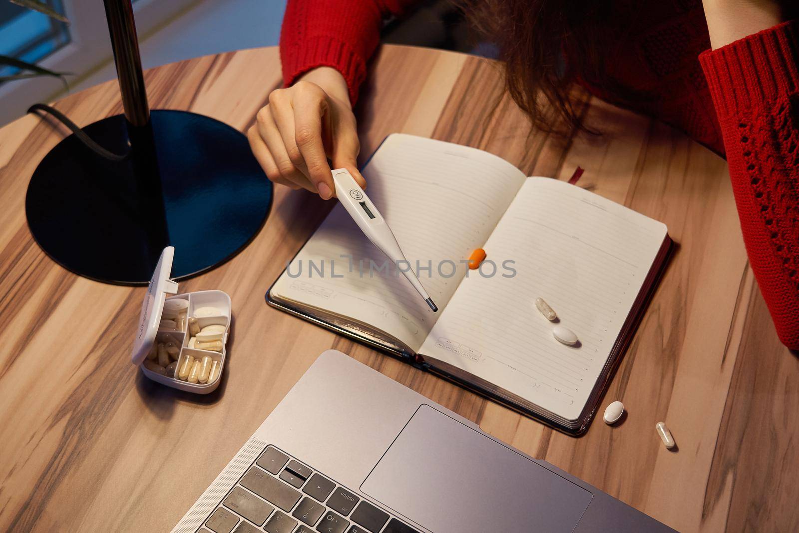 sick young woman with pills and thermometer on a table working on a laptop from home on quarantine isolation. Online work, stay home concept