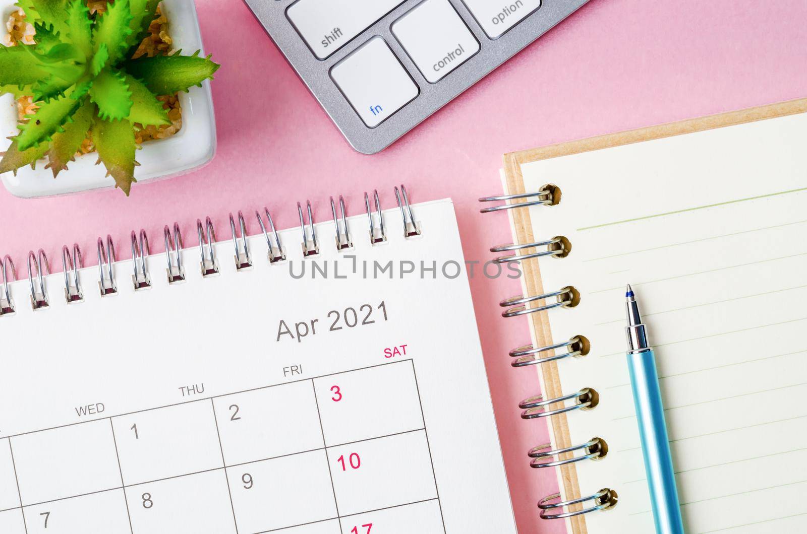 April 2021 calendar with note book on pink background.