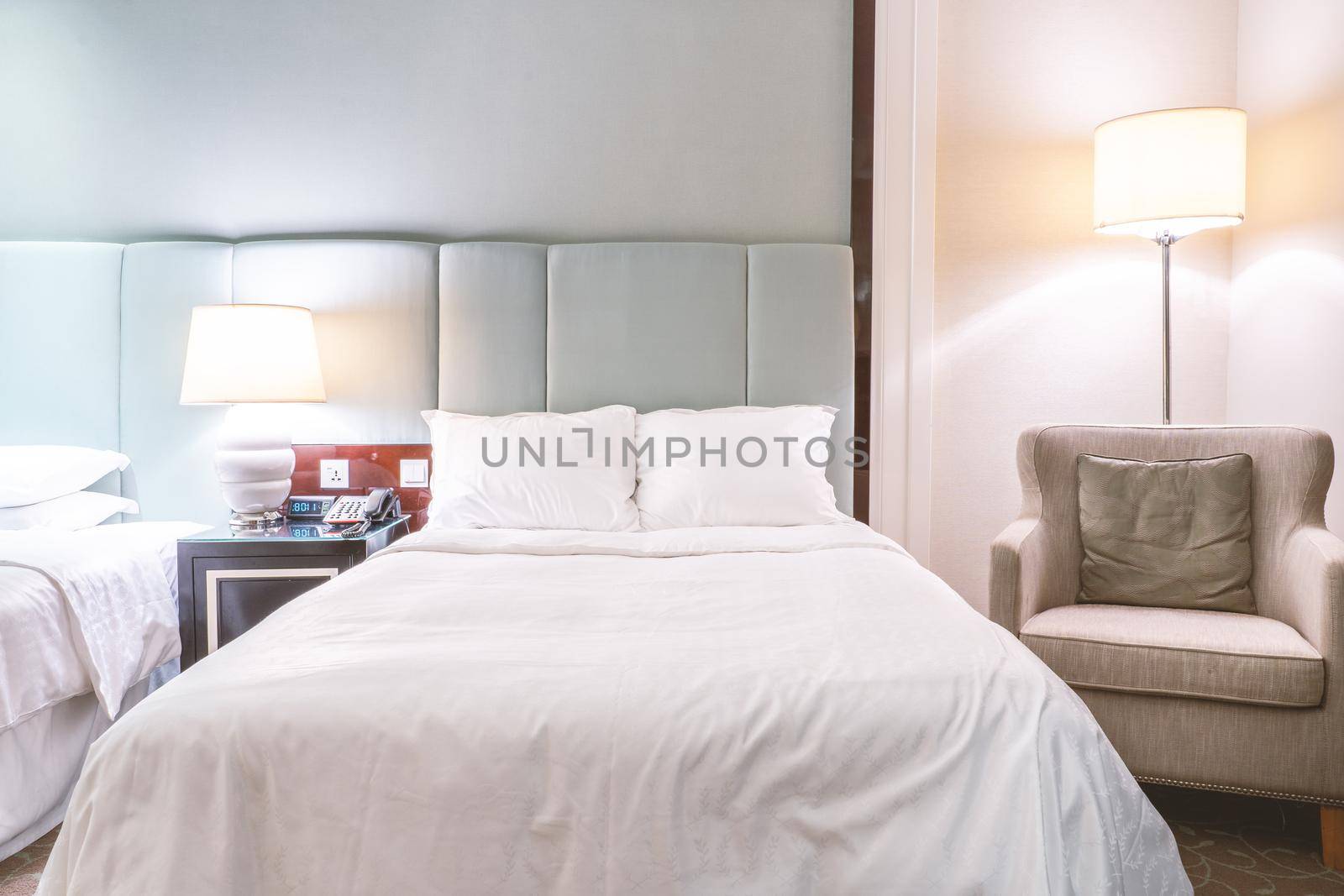 Clean and cozy modern hotel bedroom interior, warm tone room with a standing lamp, linen sofa with a cushion, design concept of luxury travel, close up.