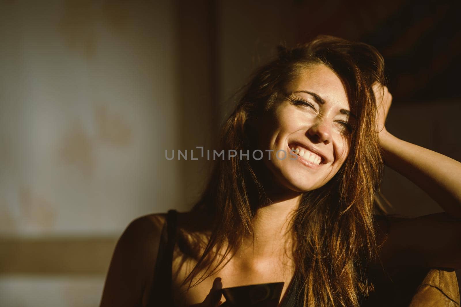 A young happy woman pensive sitting, relaxing and enjoying a sunny morning in the room.