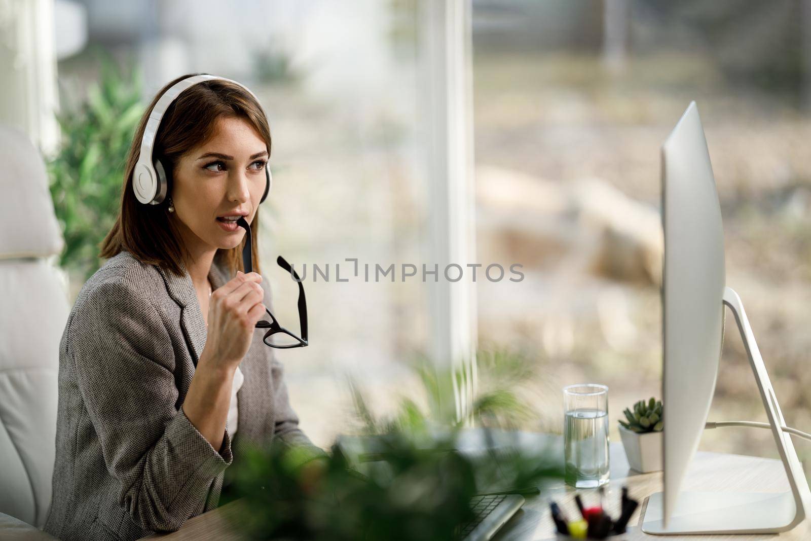 An attractive business woman sitting alone in her home office with headphones and working on computer.