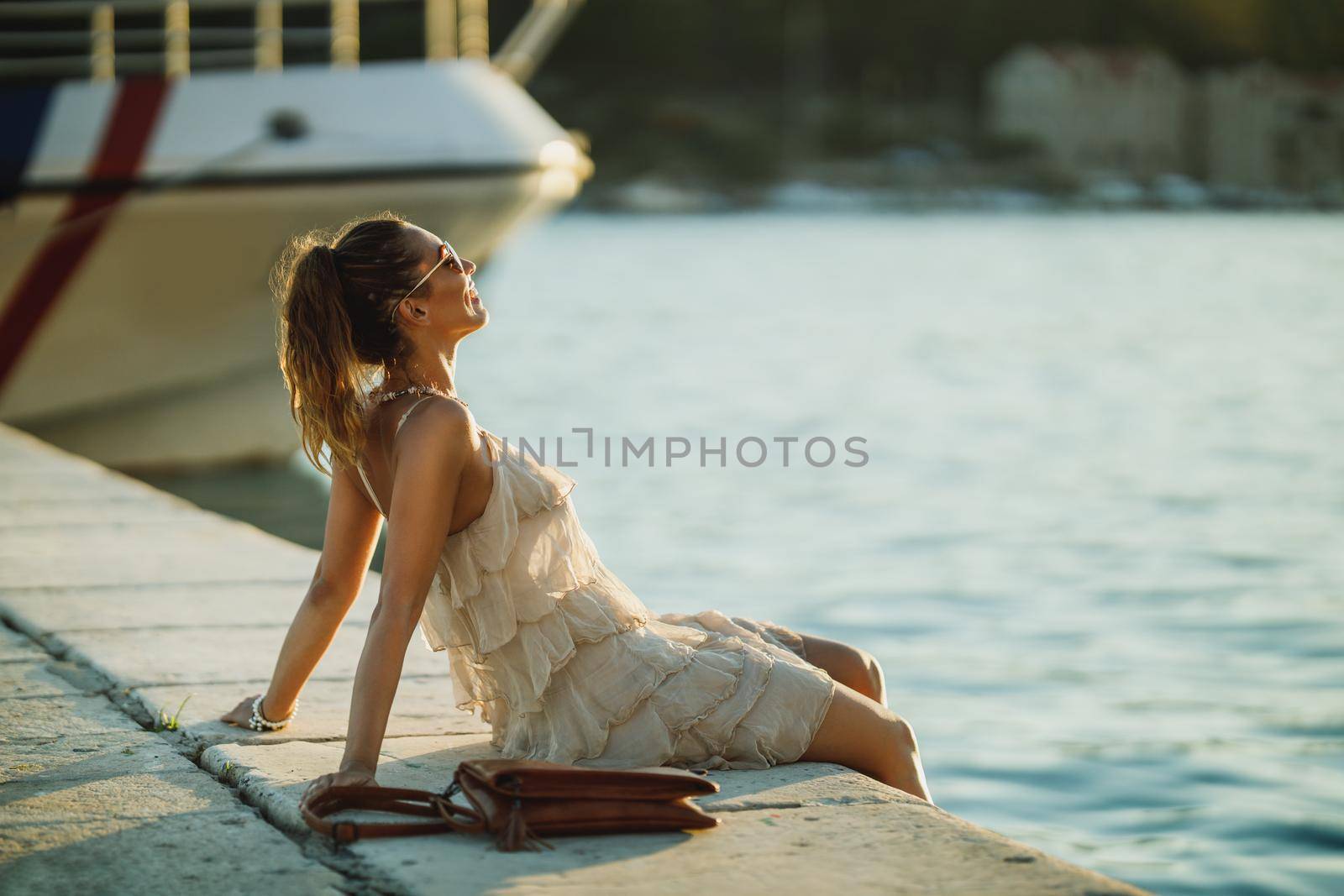 An attractive young woman sitting near the wonderful seaside of Mediterranean while enjoying a summer vacation.