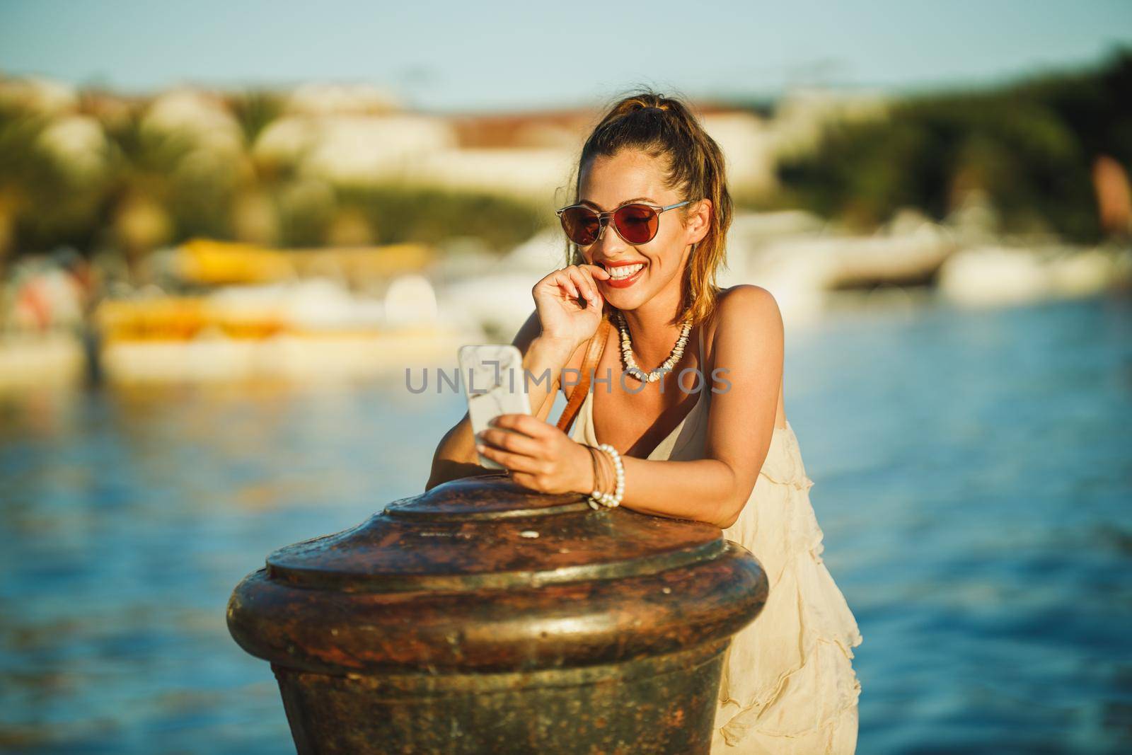 Shot of a young woman typing message her smartphone while exploring the wonderful seaside of Mediterranean.