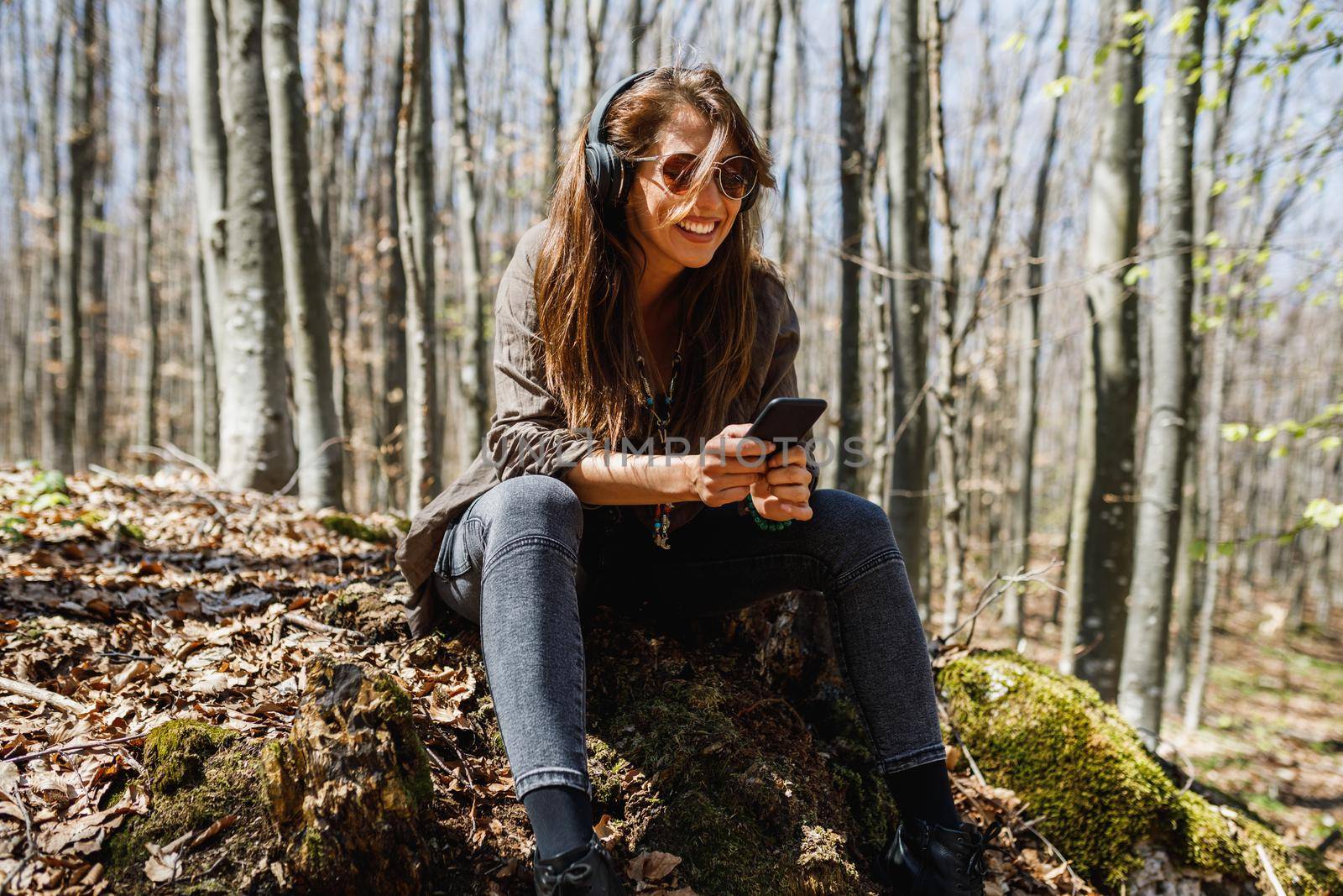 A smiling young woman using her smartphone and listening music while enjoying in nature.