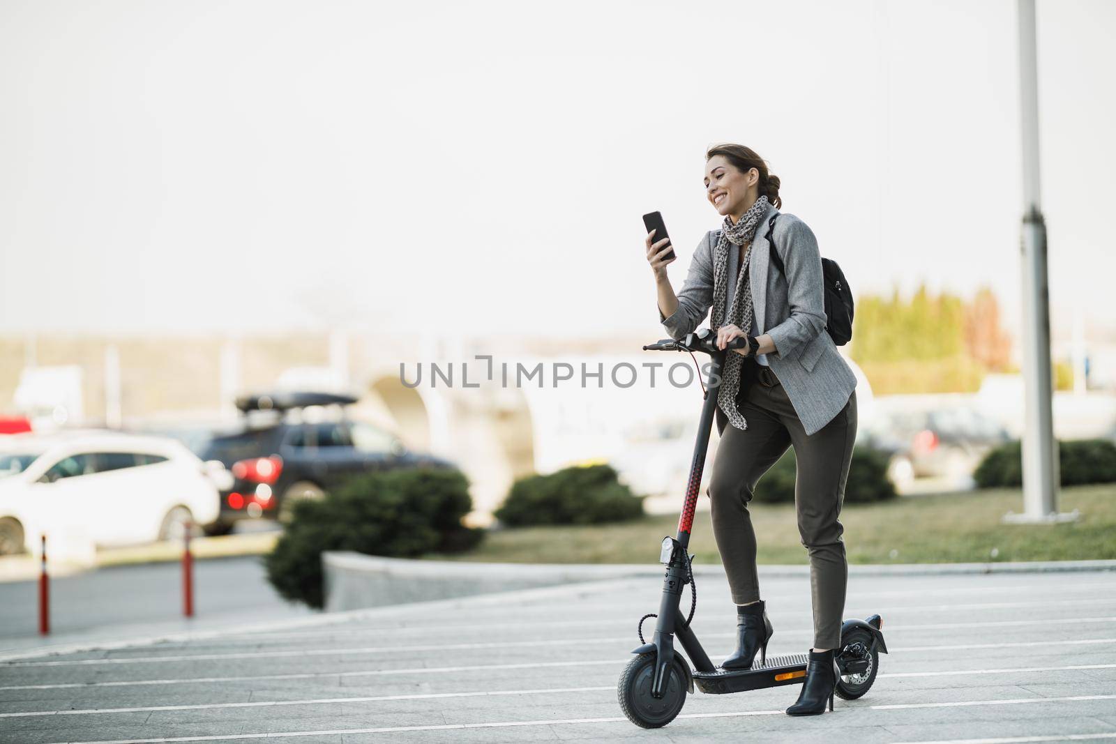 A young businesswoman with an electric scooter going to work and using her smartphone.