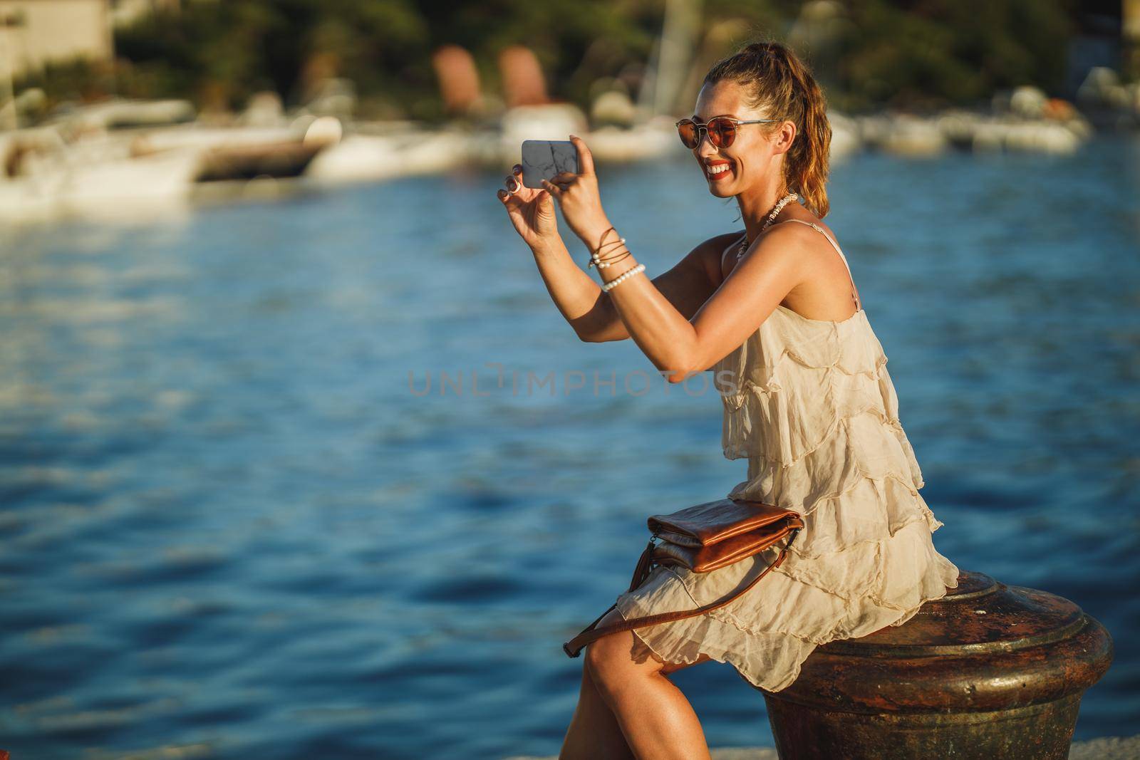 Shot of a young woman taking photos with her smartphone while exploring the wonderful seaside of Mediterranean.