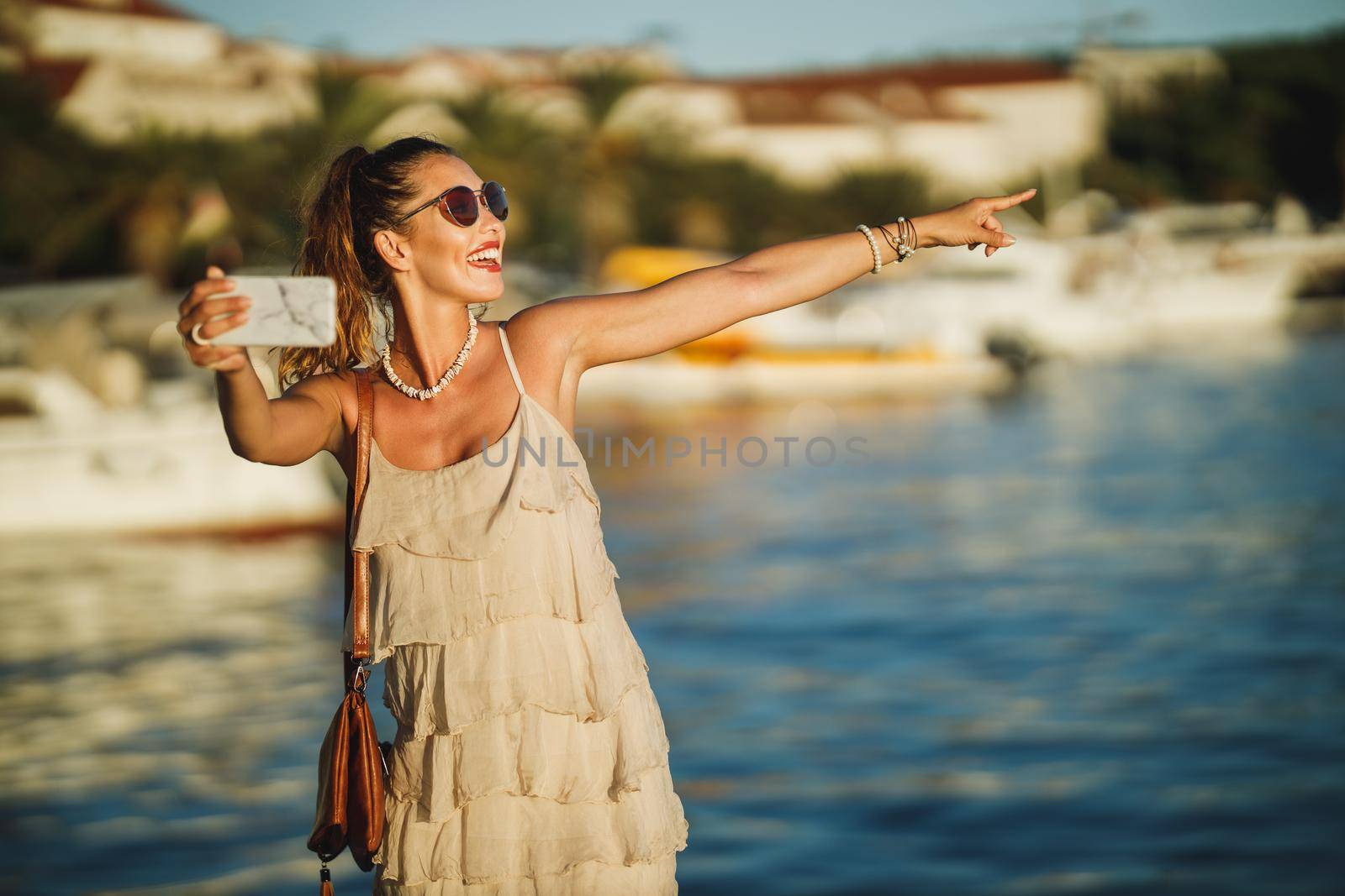 Shot of a young woman making video call with her smartphone while exploring the wonderful seaside of Mediterranean.