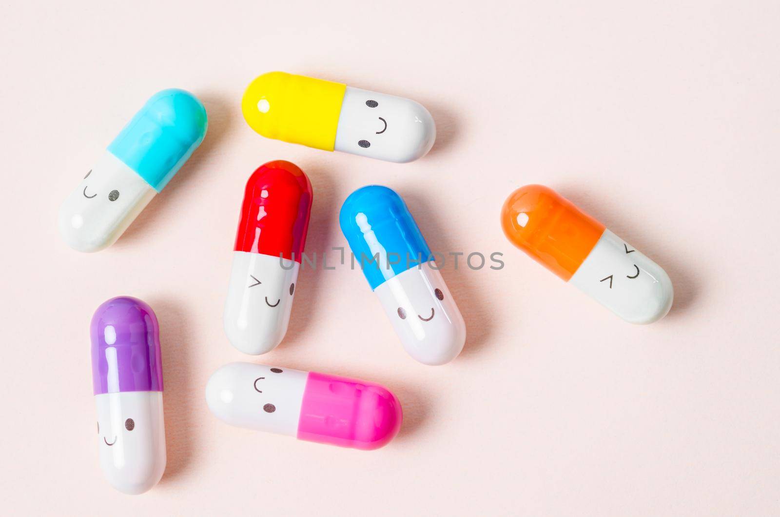 Many colorful pills capsules on pink background.