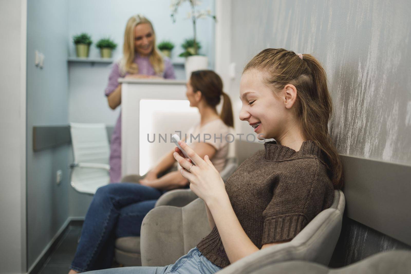 A cute teenager girl using her cellphone while waiting for medical exam at dentist.