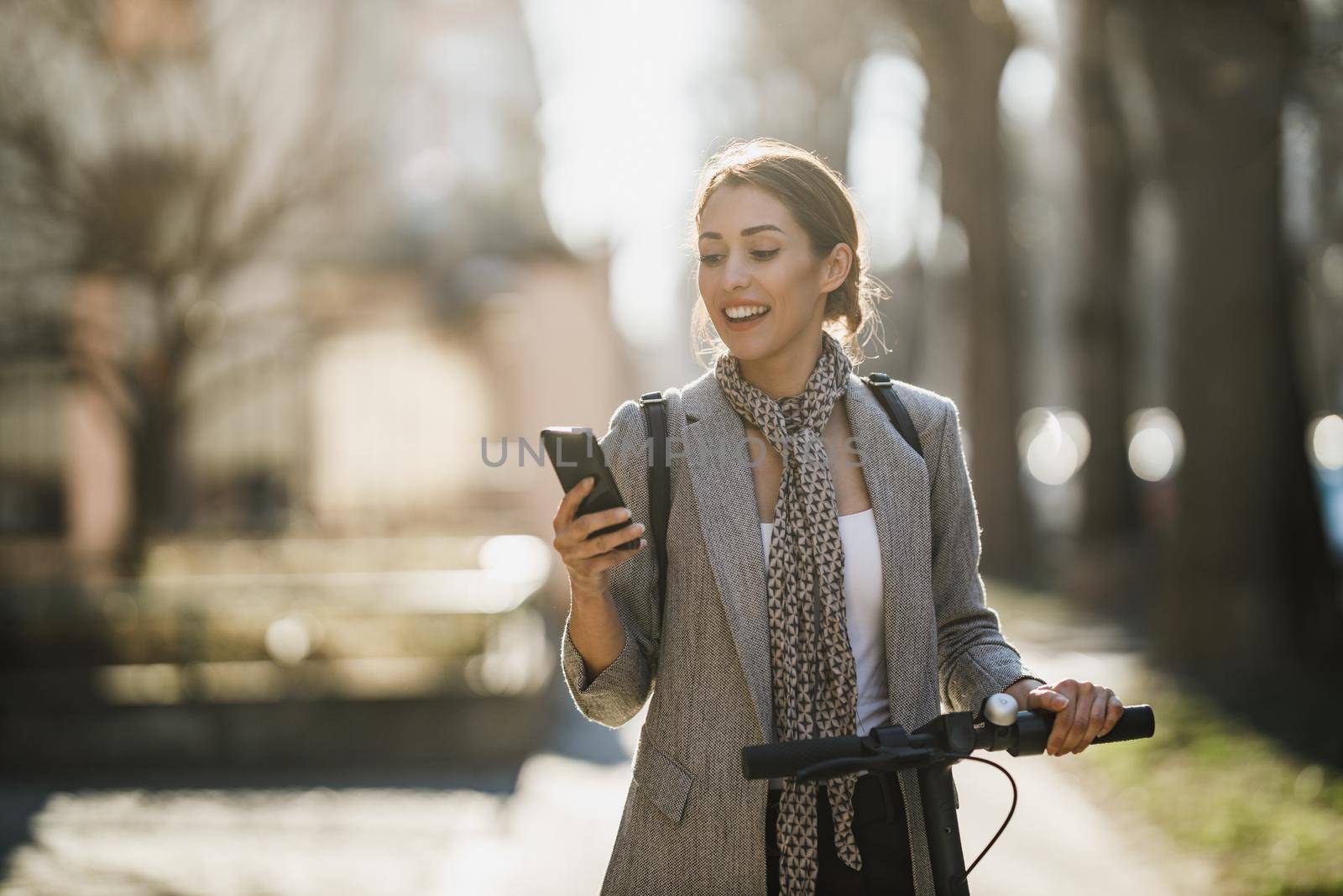 A young businesswoman riding an electric scooter and using smartphone on her way to work through the city.