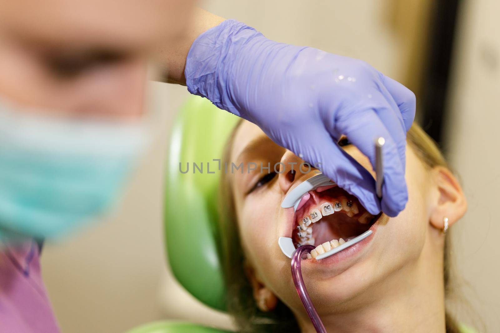 Teenage girl is at the dentist. She sits in the dentist's chair and the dentist sets braces on her teeth.