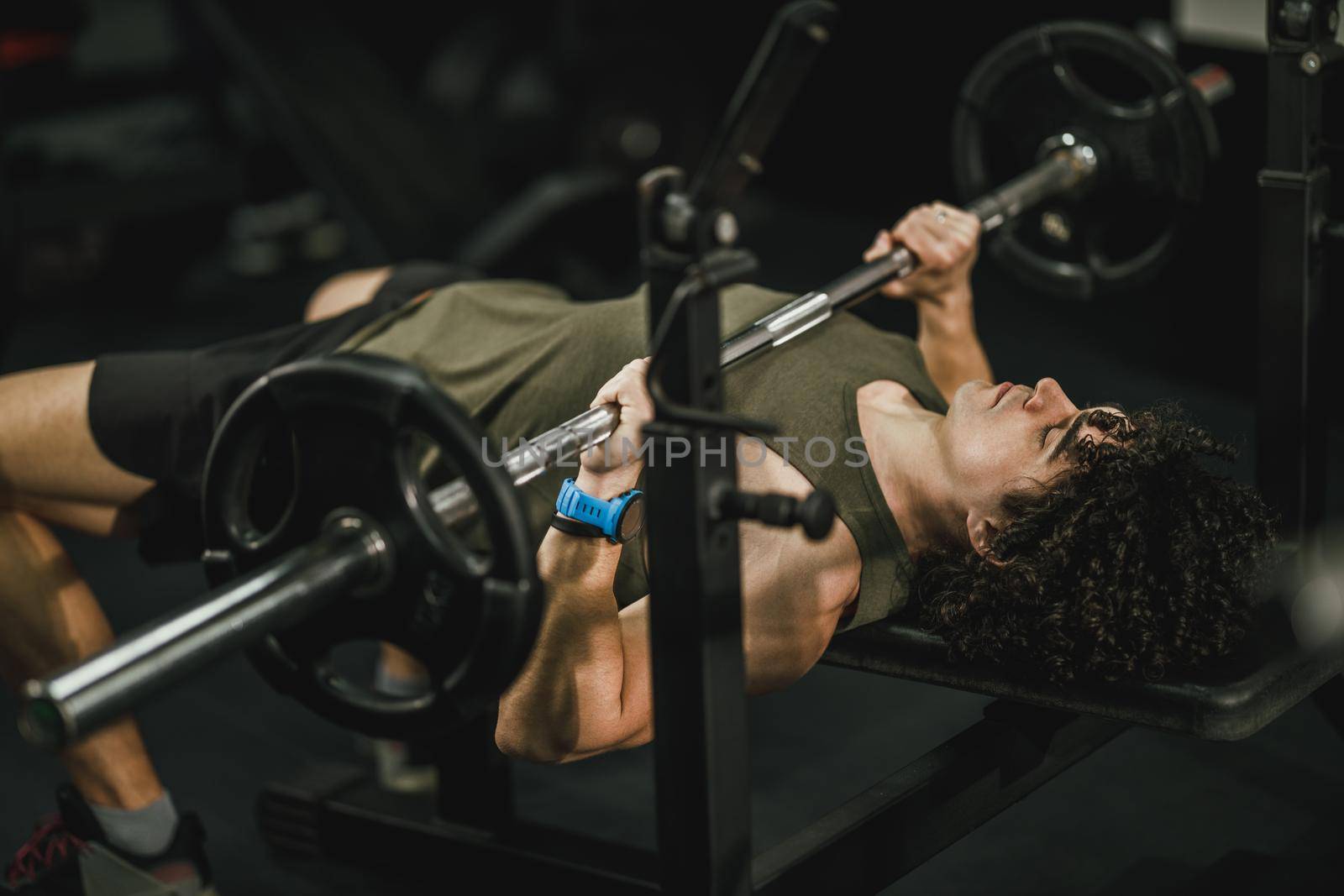 Shot of a muscular guy working out at the hard training in the gym. He is pumping up chest muscle with heavy weight.