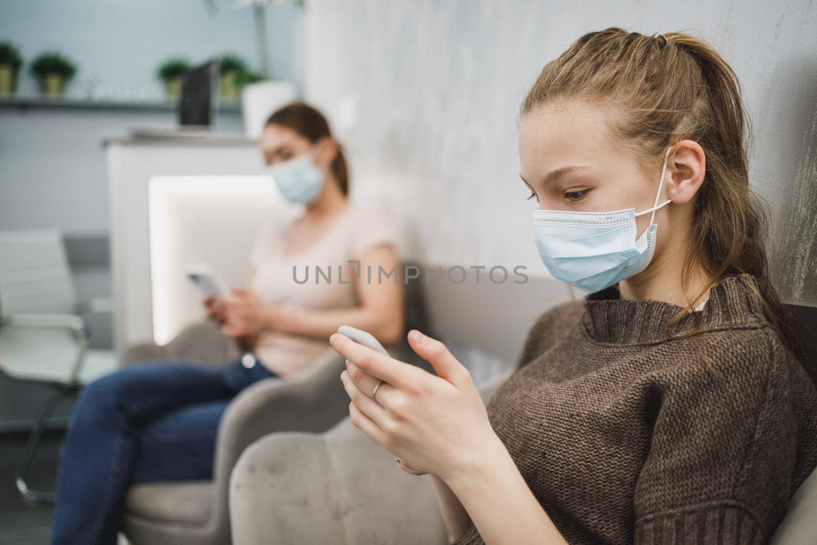 A cute teenager girl wearing face mask and using her cellphone in waiting room at dentist's office.