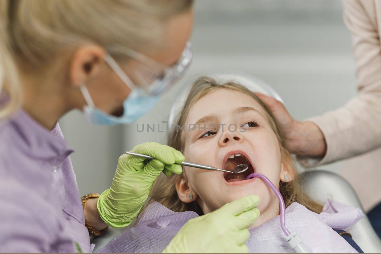 A female dentist examining cute little girl's teeth during dental procedure at dentist's office.