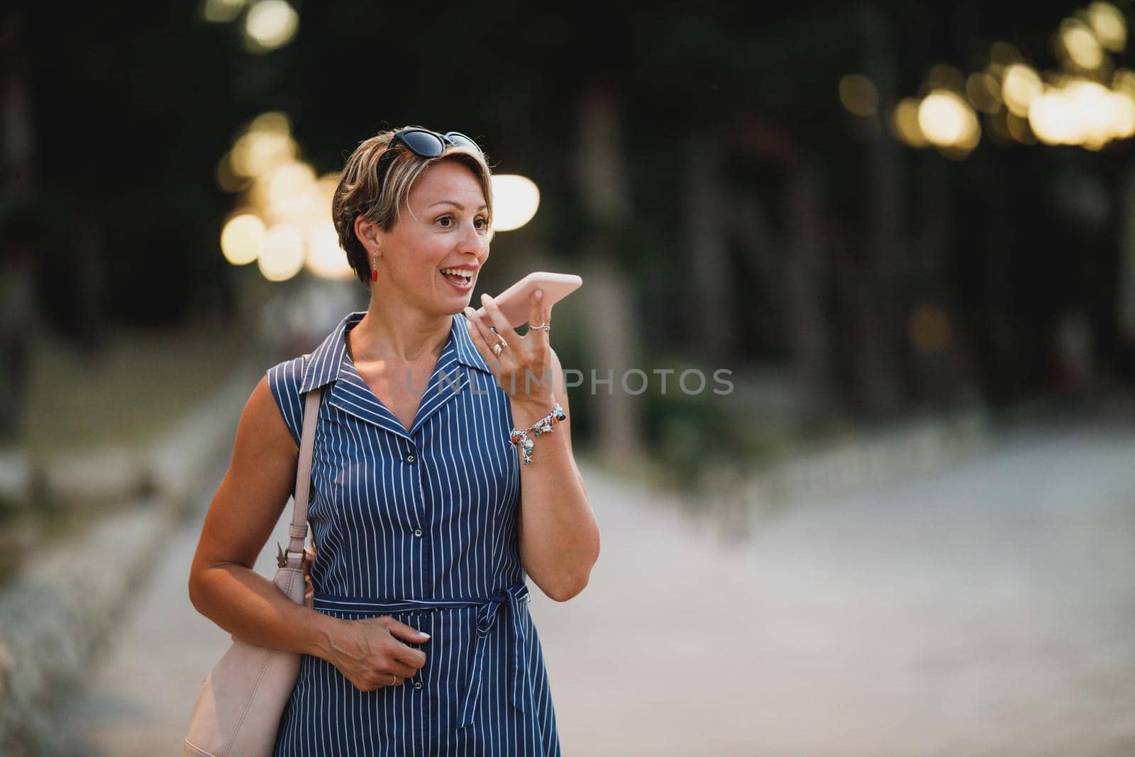 Mature attractive woman using a smartphone and enjoying a summer night walk.