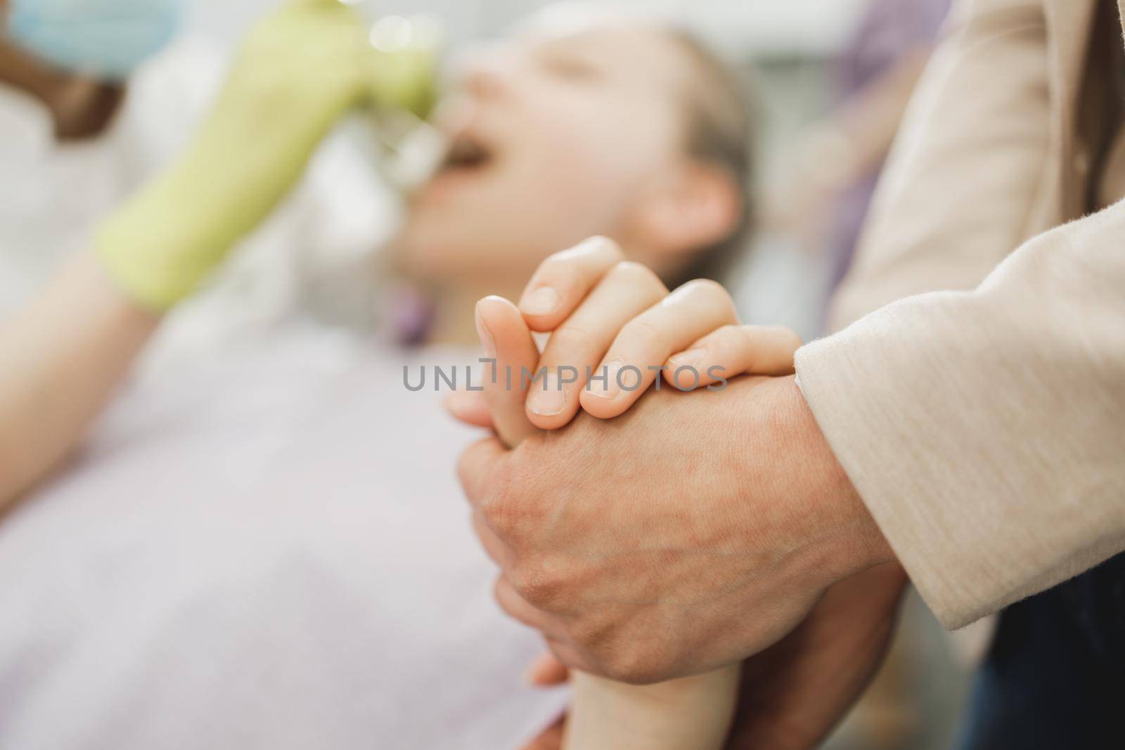 Close-up of a caring mom holding little girl's hand and encouraging and consoling her during appointment at dentist's office.