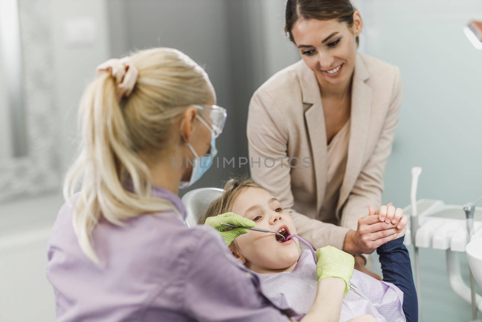 A cute little girl with her mom getting her teeth checked by dentist at dental clinic.