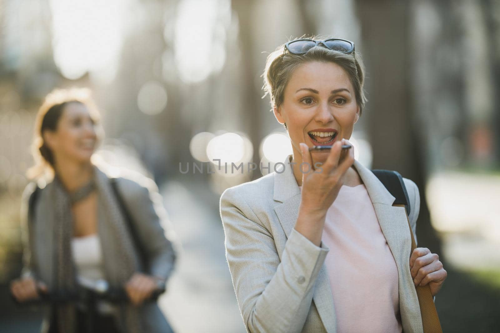A smiling mature business woman talking voice message on a smart phone on her way to work.