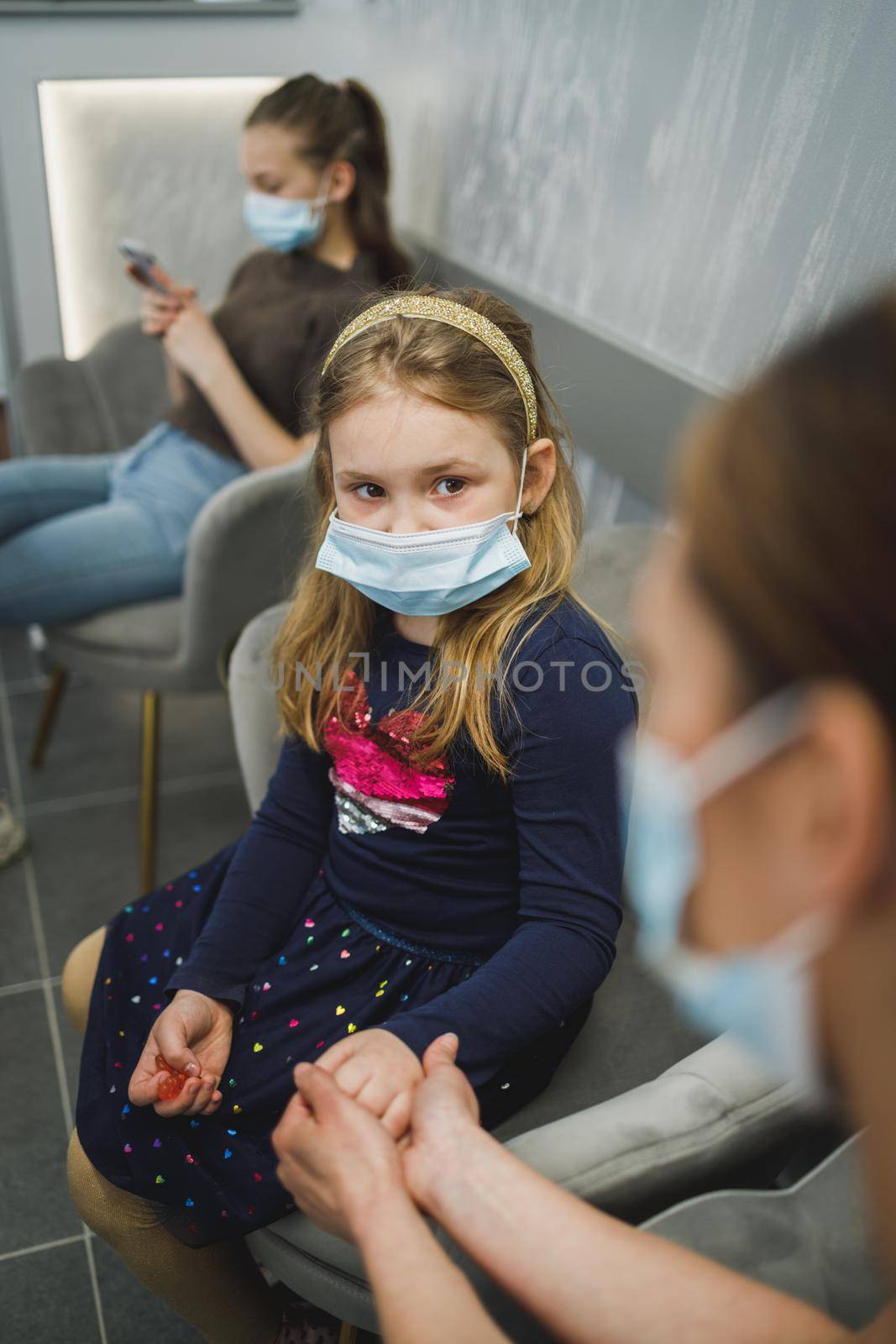 Scared little girl and her mom with face mask in waiting room at dentist's office.