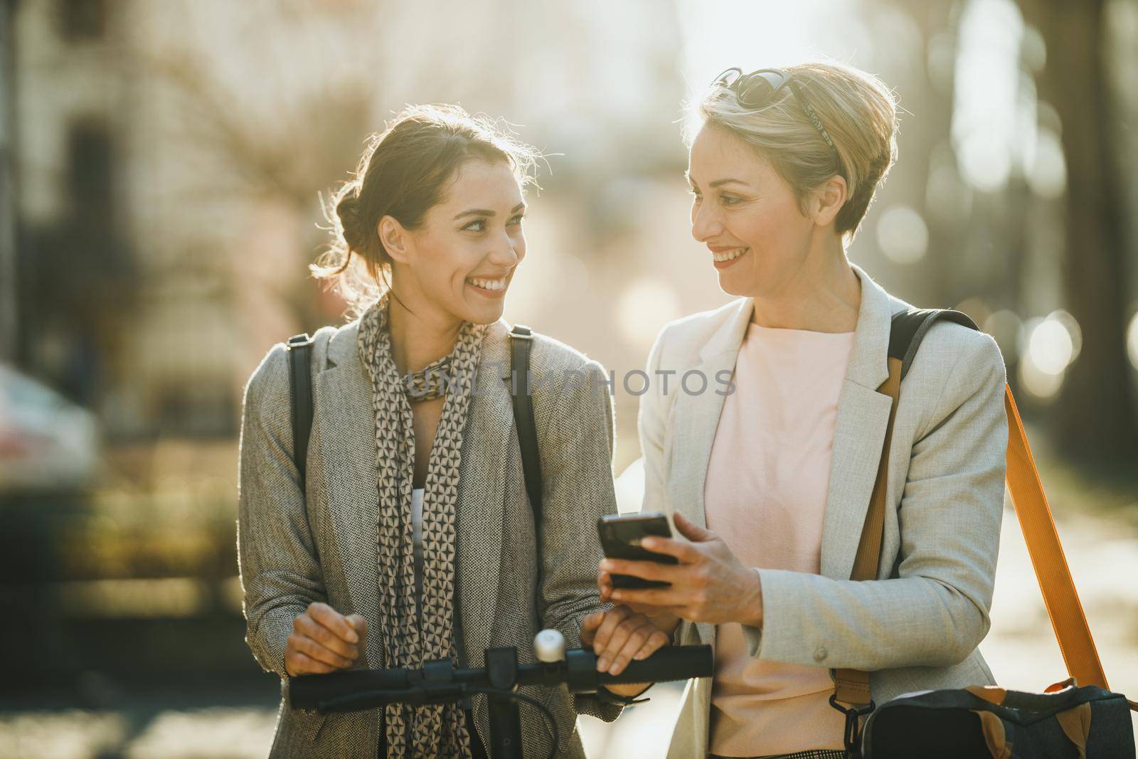 A two successful businesswomen using a smartphomne while having a quick break and walking through the city.